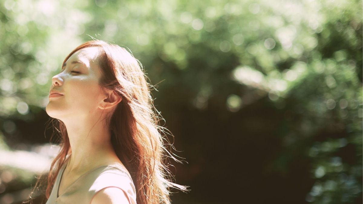 森の中で目を閉じて深呼吸し、自分の感覚に意識を向ける女性