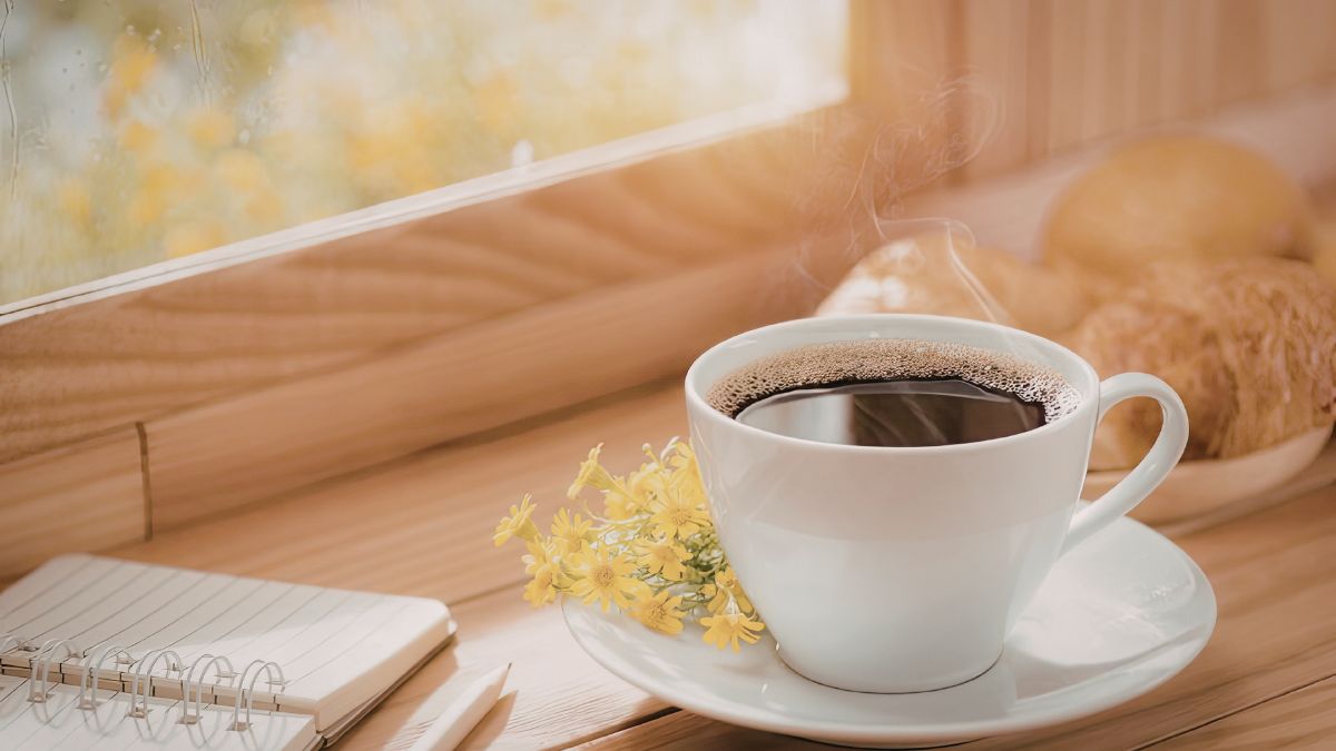 明るい窓辺に置かれたコーヒーカップと手帳と小花